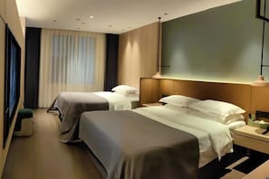 A hotel room with two beds, a bedside table, a lamp, and a large window with curtains.