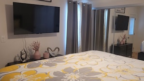 Un dormitorio con cama, televisor de pantalla plana en la pared, cómoda y espejo.