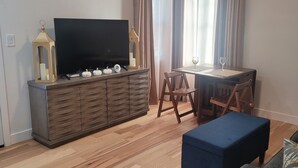 Una sala de estar con un televisor sobre un mueble de madera, una mesita con dos sillas y un sofá.