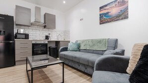 A modern kitchen with a microwave, oven, and coffee maker. There is a gray sofa with a blanket and pillows. A painting of a landscape is on the wall. - Roof Terrace | W/M | Smart TV | Free Parking (Old Swan)