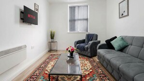 Un salon moderne avec un canapé gris, une table basse et un téléviseur fixé au mur.