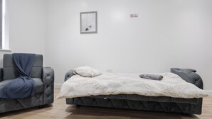 Une chambre à coucher moderne avec un lit recouvert d’un tissu gris, un fauteuil gris et une petite table de chevet.