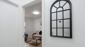Una habitación con ventana de marco negro, un sofá color crema y una mesa de centro con un jarrón.