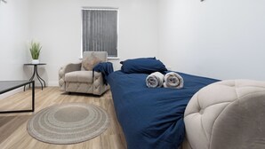 Un dormitorio con cama, una silla, una mesita y una planta en maceta.