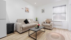 A modern living room with two sofas, a coffee table, a trash bin, and a window with blinds.