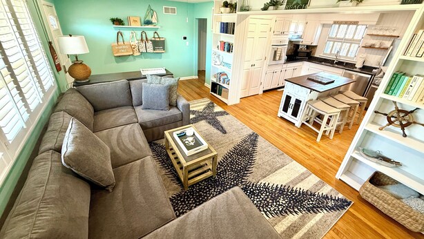 A modern living room with a sofa, coffee table, and a kitchen area with white cabinets and a dining table.