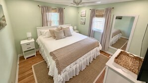 A bedroom with a bed, nightstands, a ceiling fan, a large mirror, and a window with curtains.