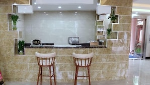 A reception area with a marble wall, two wicker chairs, a reception desk, and potted plants. - Labor Model Resort (Shanghai)