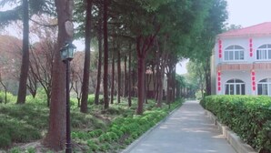 A pathway lined with trees and a building with a red roof and white walls. - Labor Model Resort (Shanghai)