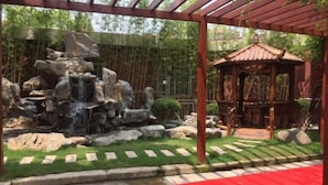 A garden with a rock waterfall, a wooden gazebo, and a red carpet path. - Labor Model Resort (Shanghai)