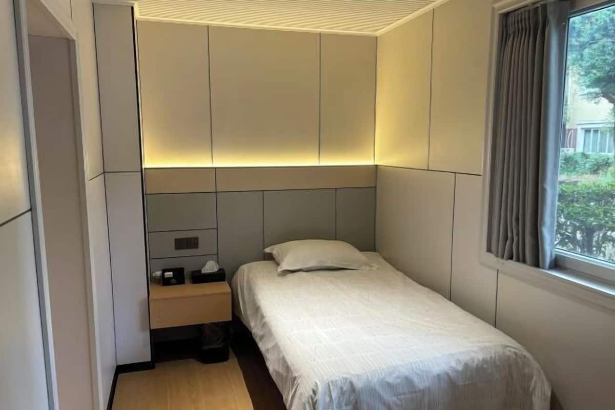 A small, modern bedroom with a single bed, a nightstand, and a window with curtains.