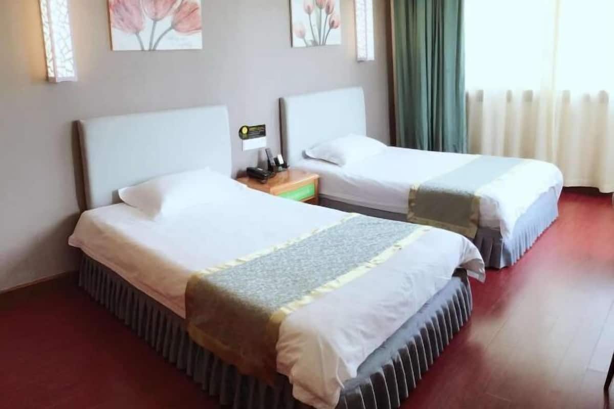 A hotel room with two beds, a nightstand, a lamp, and artwork on the wall.