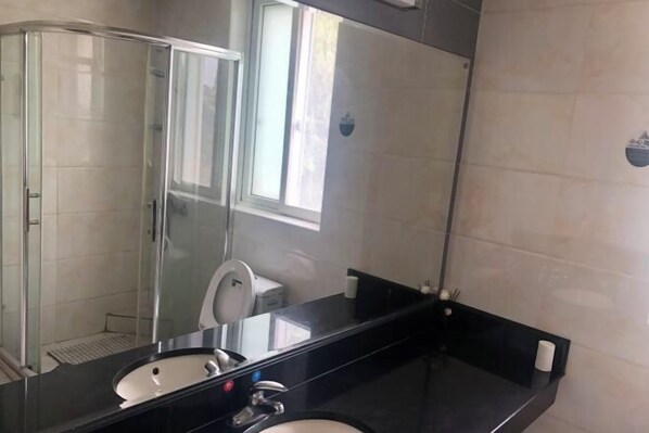 A bathroom with a glass shower enclosure, a sink with a mirror, and a toilet. - Labor Model Resort (Shanghai)