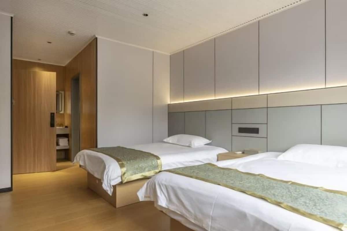 A hotel room with two beds, a wooden wardrobe, and a modern ceiling design.