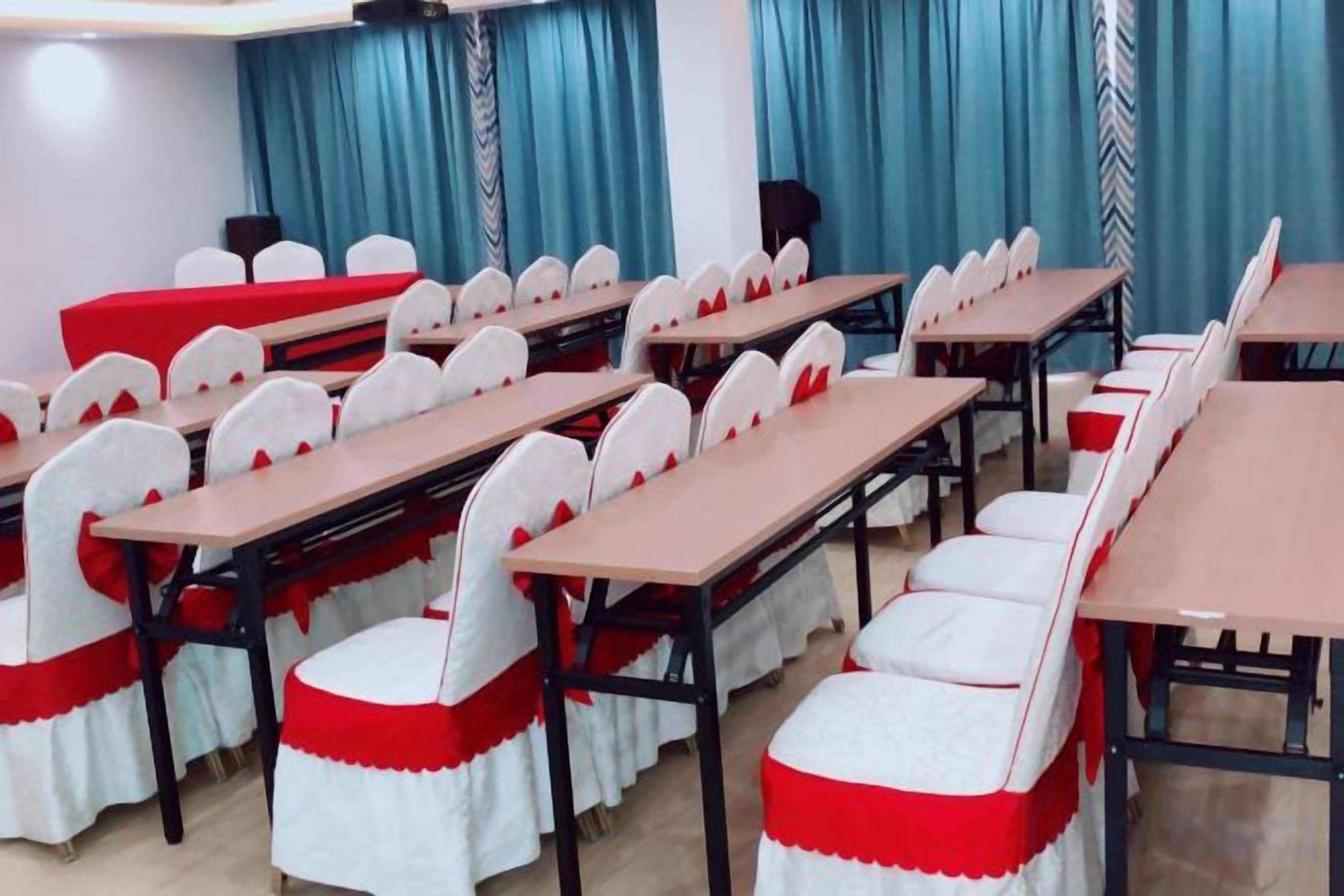 Un salón de conferencias con filas de mesas y sillas, cortinas azules y un papel tapiz estampado.