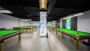 A pool hall with multiple pool tables, a central pillar with a banner, and a wall with a mural.