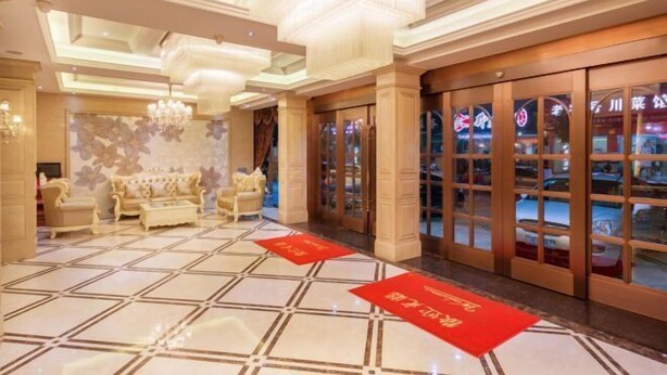 Un hall de hotel con suelo de baldosas, un conjunto de sofás, una lámpara de araña y una entrada con puerta de vidrio.