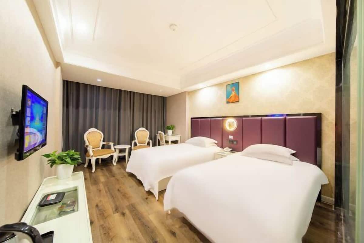 Une chambre d’hôtel avec deux lits, un bureau avec un ordinateur, une télévision et une plante.