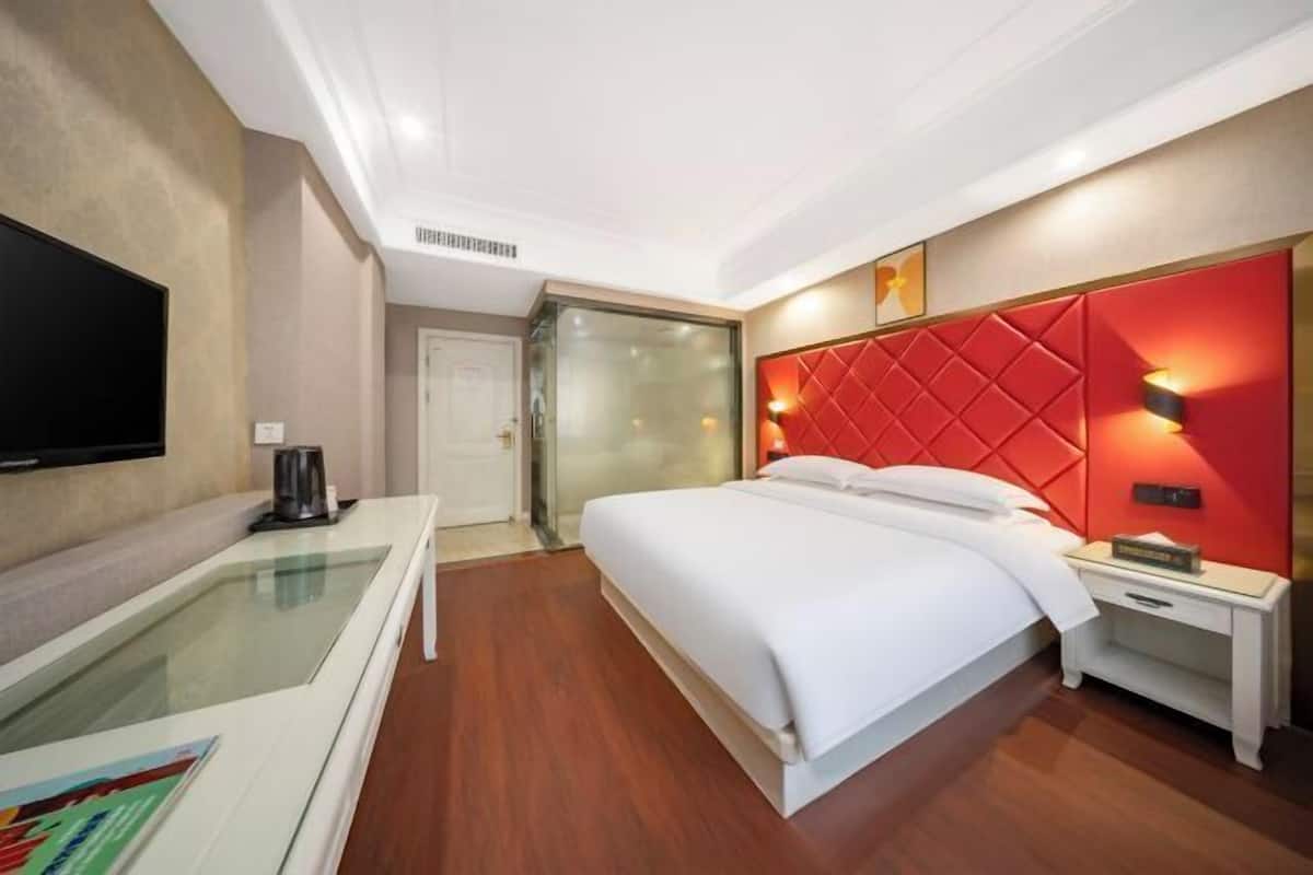 Une chambre d’hôtel équipée d’un lit, d’une table de chevet, d’une télévision et d’une cloison en verre.