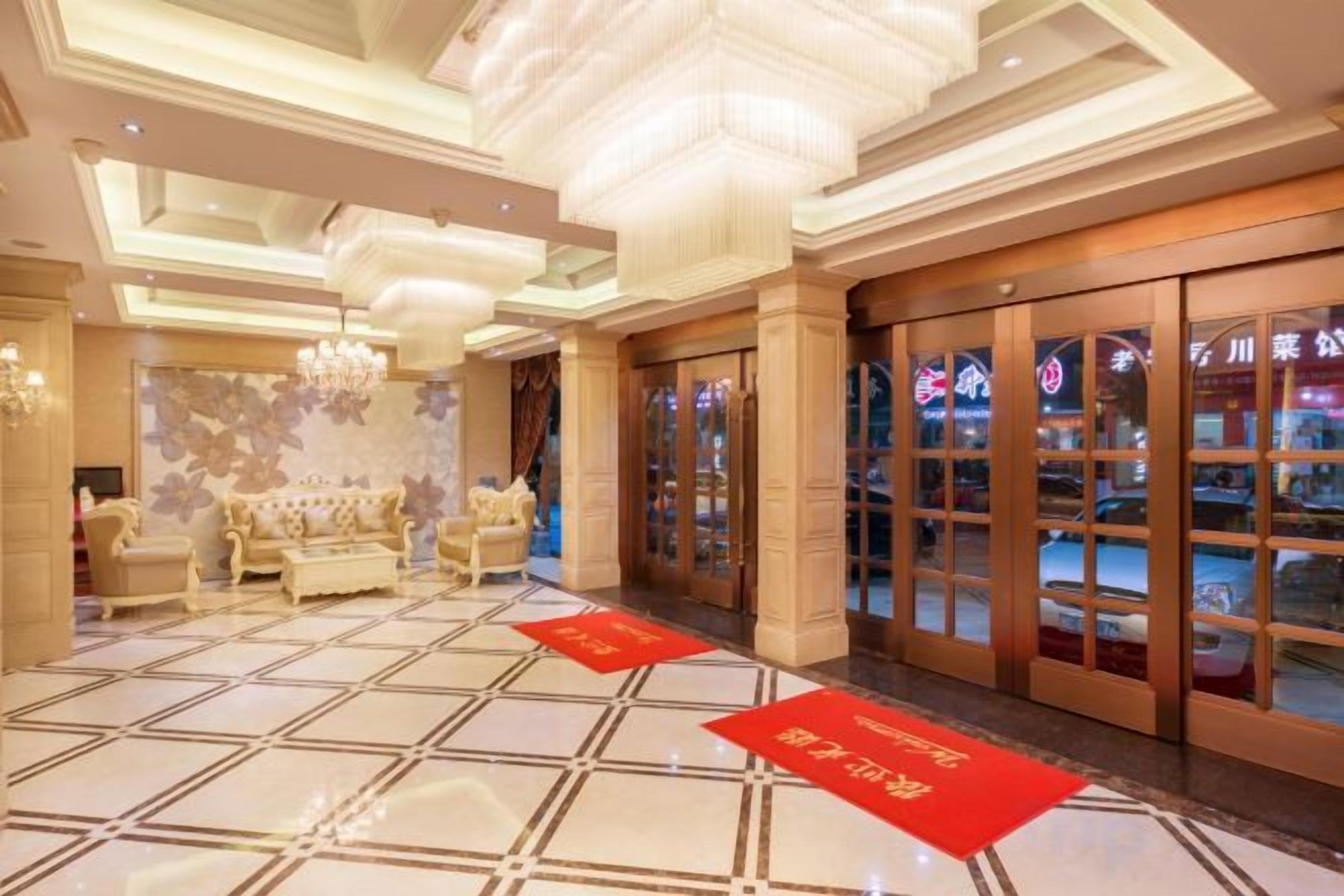 A hotel lobby with a checkered floor, a sofa, a chandelier, and a red carpet.