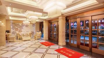 A hotel lobby with a checkered floor, a sofa, a chandelier, and a red carpet.