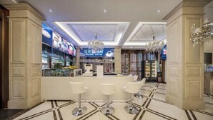 Zona de bar moderna con una cafetería al fondo, que incluye una barra, tres taburetes blancos y un suelo con diseño.