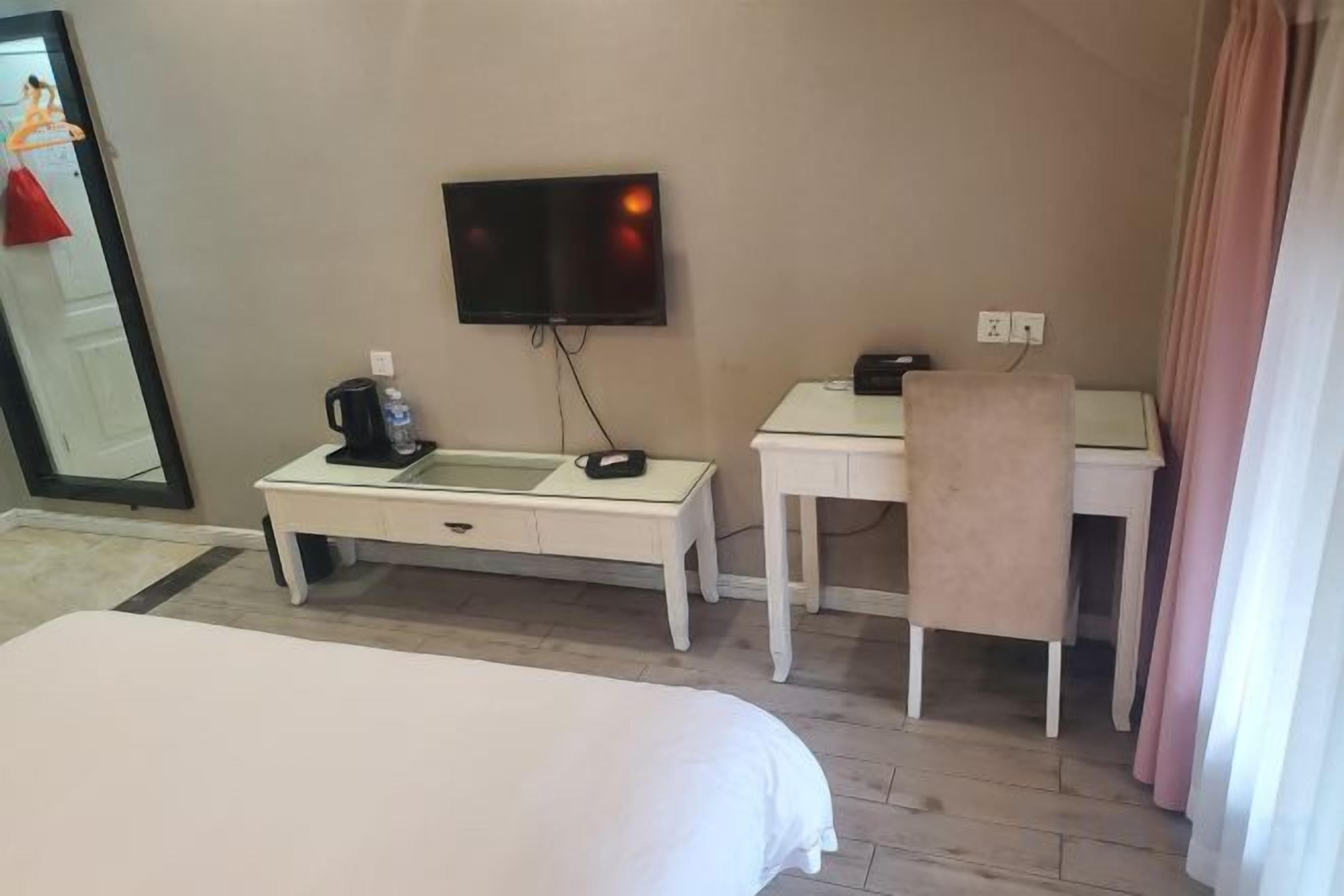 A hotel room with a bed, a desk, a chair, a television, and a mirror.