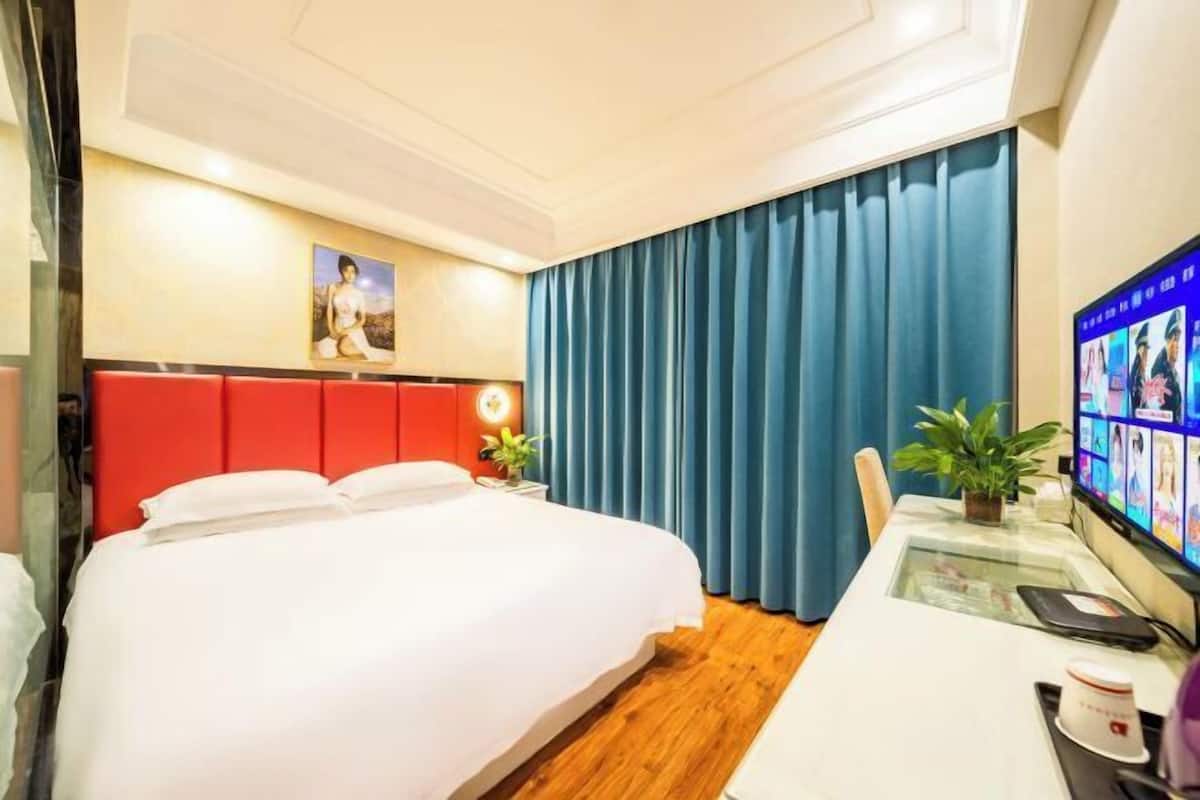 Une chambre d’hôtel avec un lit, un bureau avec un ordinateur, une télévision et une fenêtre avec des rideaux.