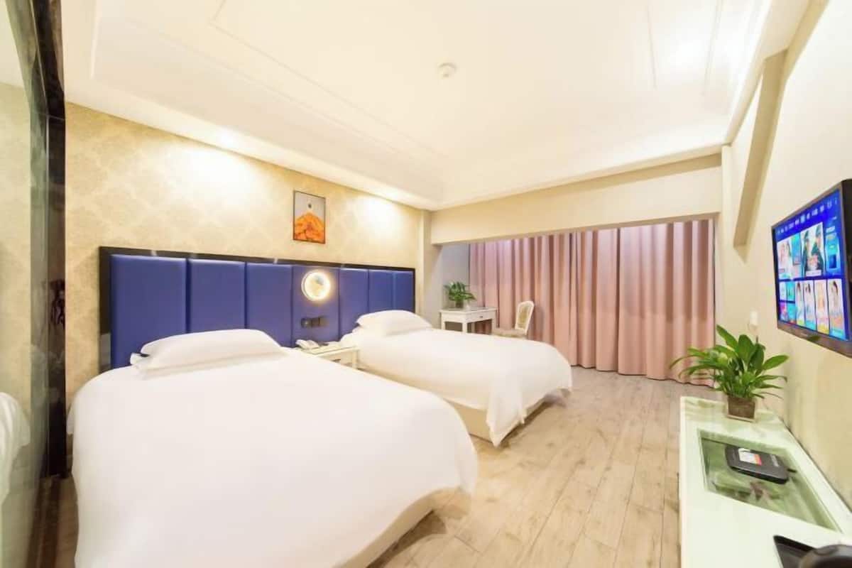 Une chambre d’hôtel avec deux lits, un bureau, une chaise, une télévision et une plante.