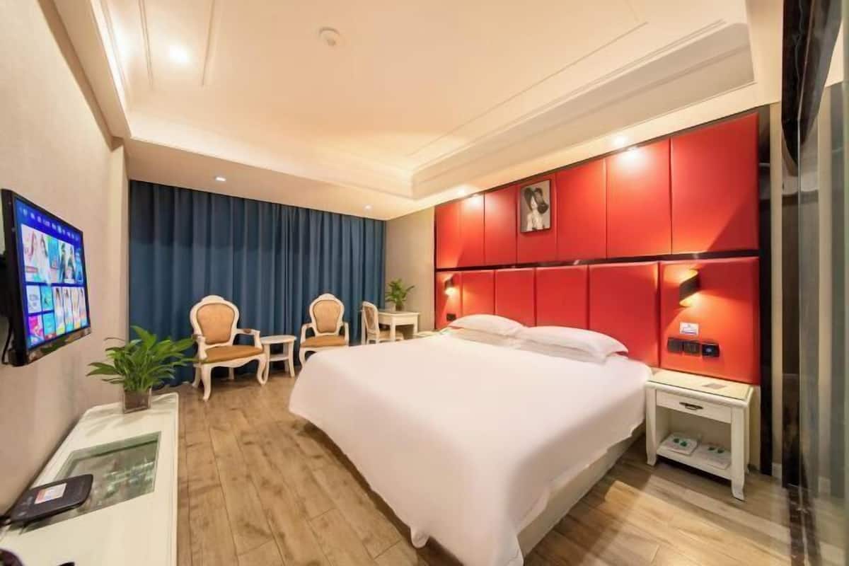 Une chambre d’hôtel équipée d’un lit, d’un bureau, d’une chaise, d’une télévision et d’un mur d’accent de couleur rouge.