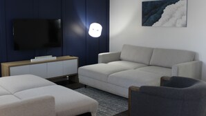 Een moderne woonkamer met een flatscreen televisie, een bank, een fauteuil en een kleine tafel.