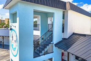 A multi-story building with a light blue exterior, a visible staircase, and a balcony with a black railing. - Mallory Squared (Siesta Key)