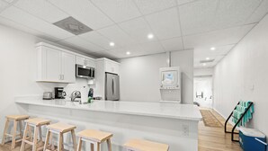 A modern kitchen with white cabinets, a stainless steel refrigerator, a microwave, and a coffee maker. There are four wooden stools at the kitchen island. - Mallory Squared (Siesta Key)