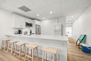A modern kitchen with white cabinets, a stainless steel refrigerator, a microwave, and a coffee maker. There are four wooden stools at the kitchen island. - Mallory Squared (Siesta Key)