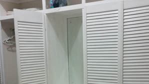 A bedroom with a bed, a white wardrobe with multiple compartments, and a small mirror.