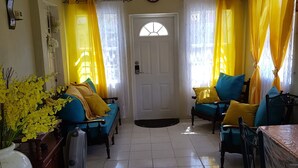 A room with a tiled floor, a ceiling fan, yellow curtains, and a white door.