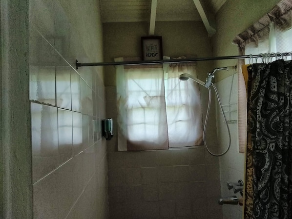 Zona de ducha con mampara de vidrio, un perchero y un cartel que dice "LATHER REPEAT".