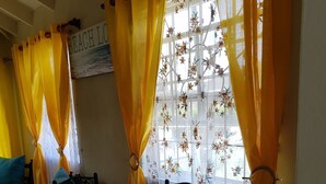 A dining area with a table covered in plastic, yellow curtains, and floral window treatments.