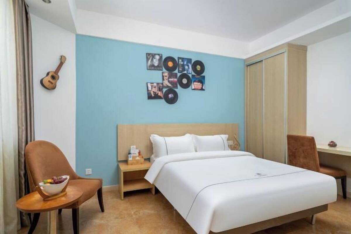 Una habitación de hotel con cama, mesita de noche, silla, una guitarra y una pared decorada con portadas de discos.