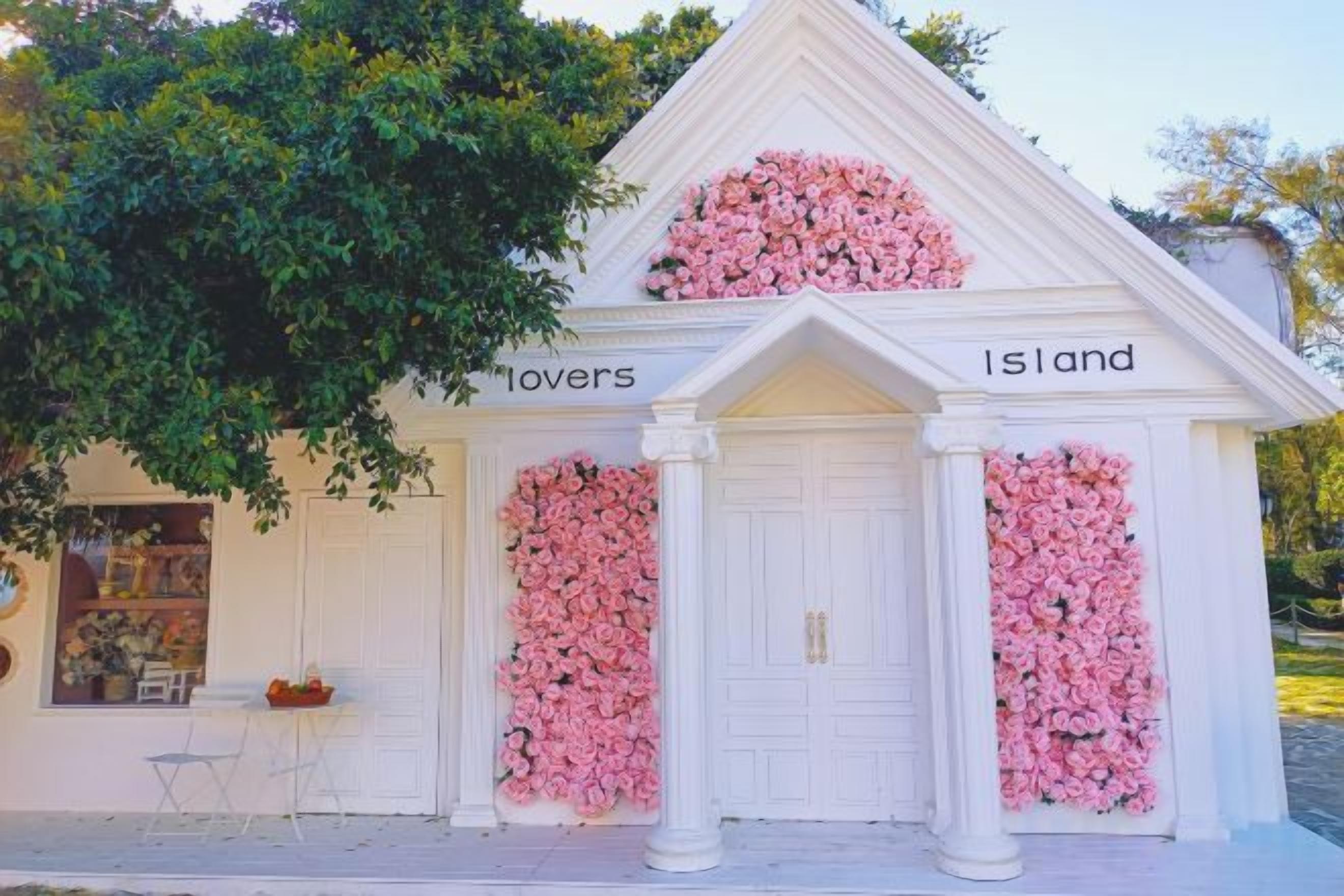 A white building with two doors, each adorned with pink floral arrangements, and the words 'lovers' and 'Island' above the doors.