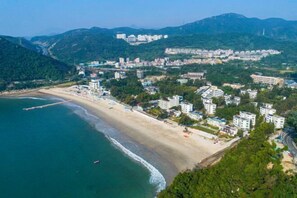 An aerial view of a coastal town with a beach, residential buildings, and a mountainous backdrop. - Shenzhen Xiyong Resort (Shenzhen)
