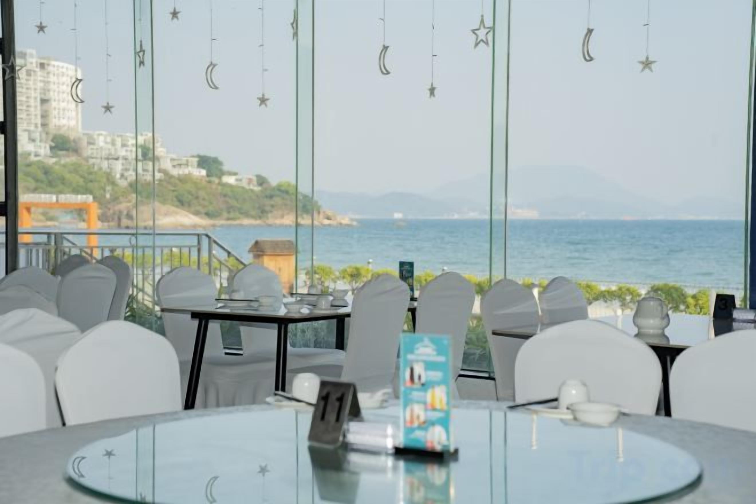 Un restaurant doté de tables et de chaises en verre, offrant une vue sur la mer et disposant d’un balcon avec une balustrade.
