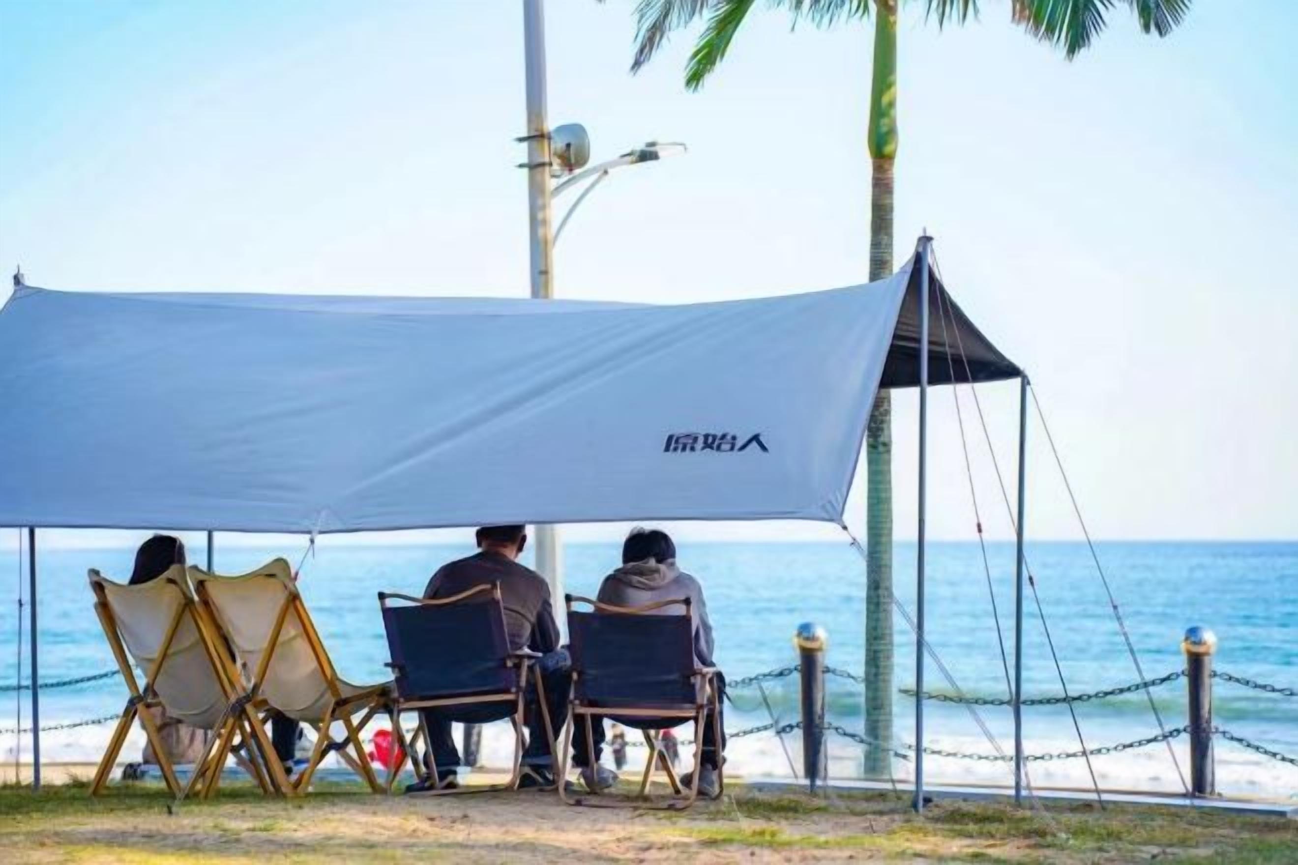 A beach scene with a tent and chairs under a canopy, overlooking the sea.