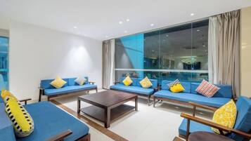 A modern living room with sofas and a coffee table, large windows with curtains, and a view of the city.