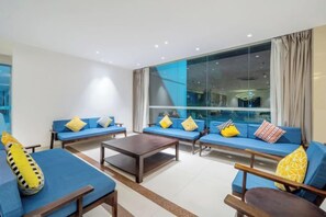 Un salon moderne avec des canapés et une table basse, de grandes fenêtres avec des rideaux et une vue sur la ville.