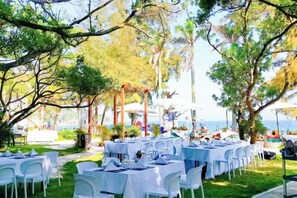 An outdoor dining area with tables and chairs, surrounded by trees and a view of the sea. - Shenzhen Xiyong Resort (Shenzhen)
