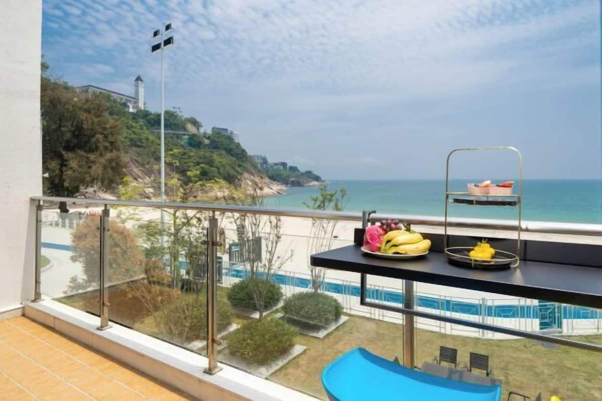 Un balcón con vista al mar, una piscina y un área de comedor con fruta.