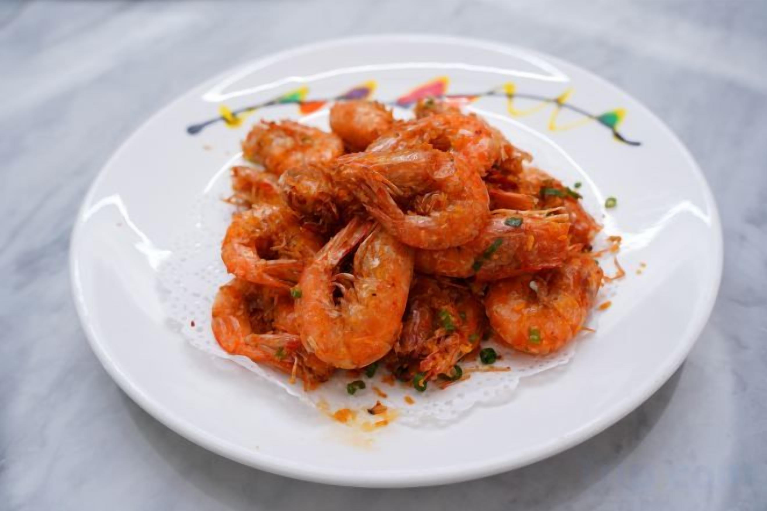 A plate of cooked shrimp on a white plate with a decorative edge.