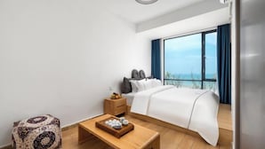 A hotel room with a bed, a wooden table with a tray of items, a patterned ottoman, and a large window with a view. - Shenzhen Xiyong Resort (Shenzhen)