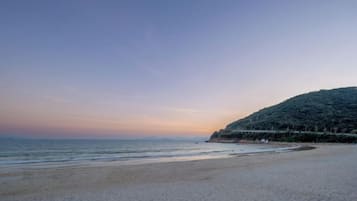 A beach with a gentle slope leading to the water, a clear sky, and a distant hill with vegetation.